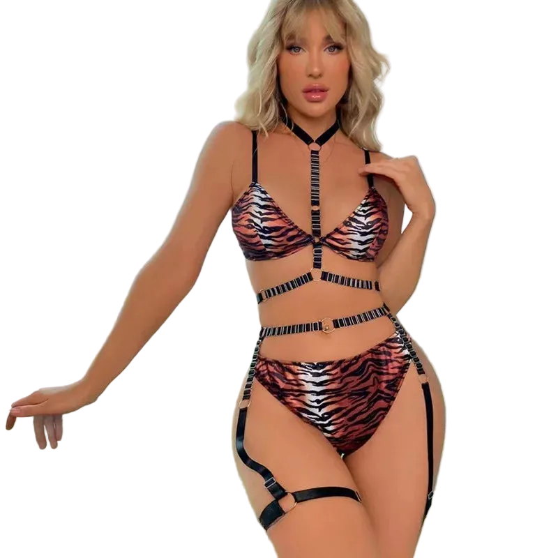 A woman modeling a tiger-print strappy bikini set with matching garter straps, standing by a large window with a city view.