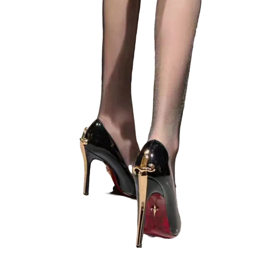 A close-up of a person wearing glossy black patent stiletto pumps with gold-tone hardware and red soles, standing on a light gray tiled floor.