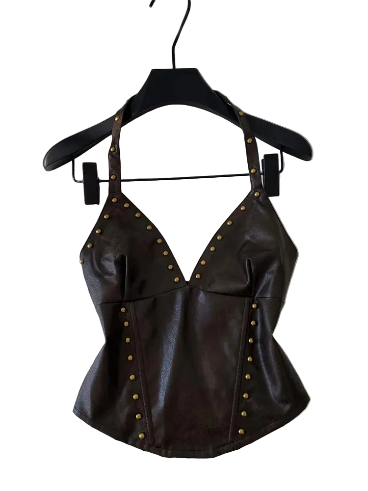 A dark brown faux-leather halter top with gold-tone studs, hanging on a black hanger against a white wall with some desk items visible in the background.