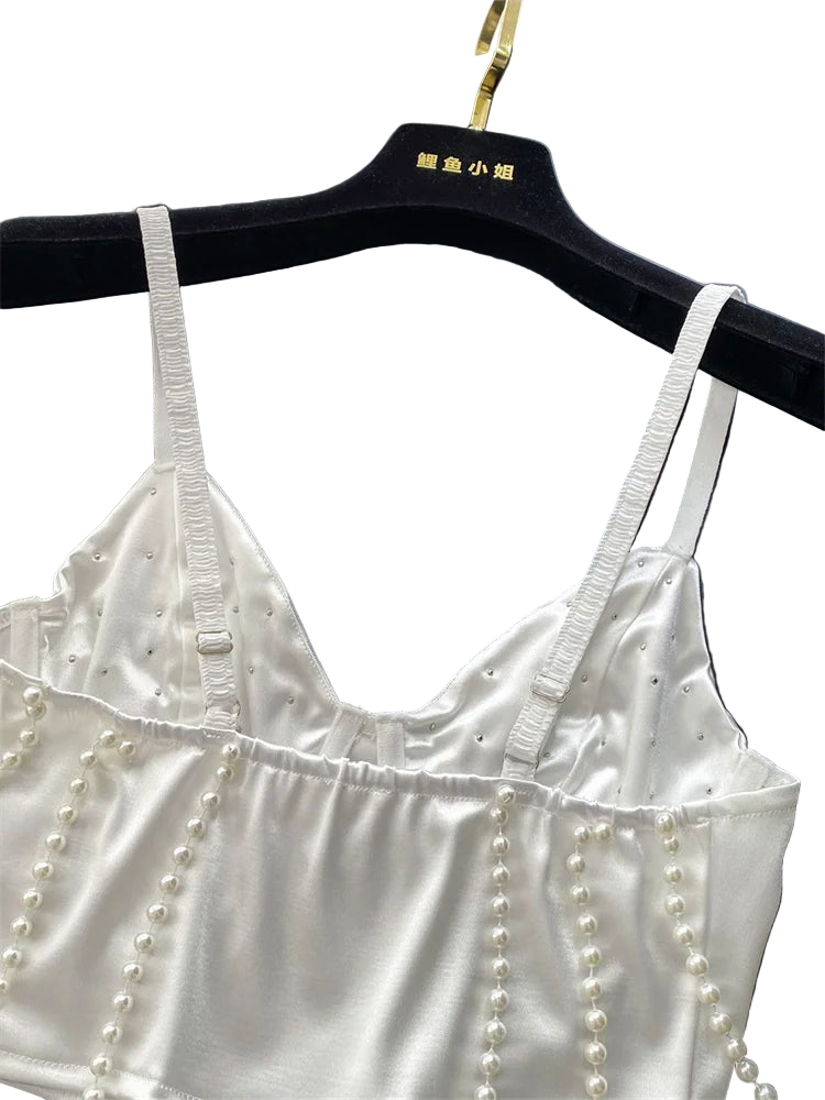 White satin top with pearl embellishments on a black hanger against a gray background.