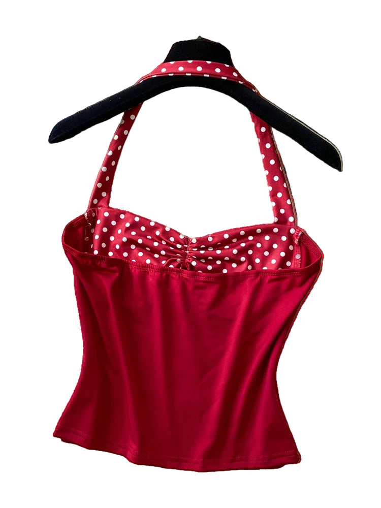 Red polka dot top on a hanger with a straw hat and pearl necklace on a textured surface.