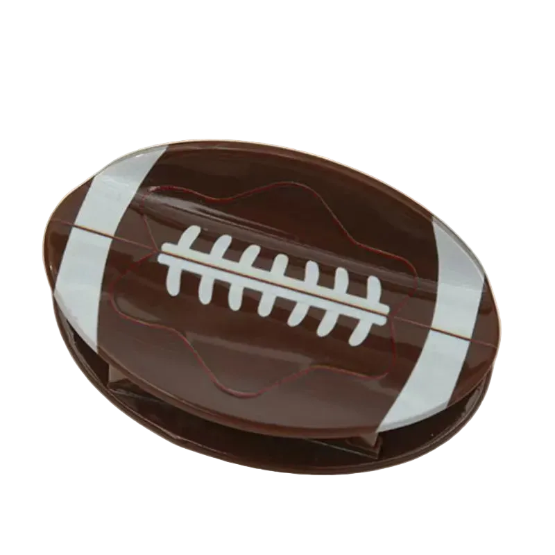 A football-shaped chocolate bar or candy bar in glossy dark brown with white laces and white side stripes, photographed on a plain light beige background.