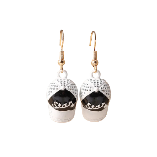 A pair of dangling earrings shaped like baseball caps, with white textured caps featuring black front panels and gold fishhook wires, displayed on a beige jewelry stand.