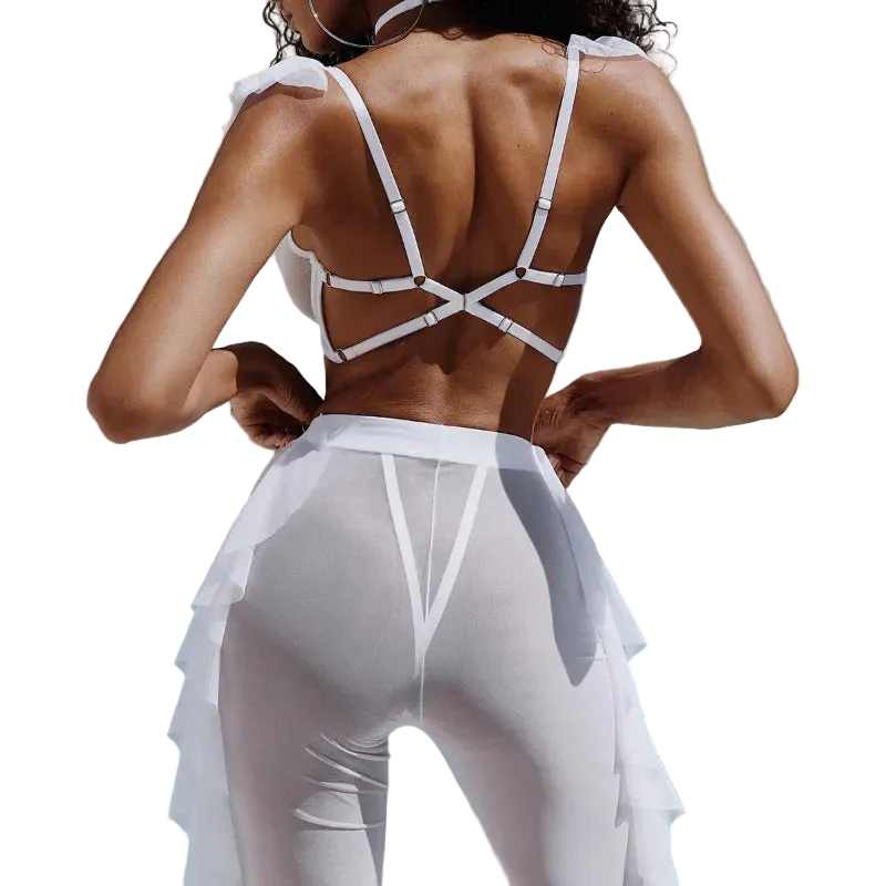 A woman shown from behind wearing a white strappy bikini top and matching white ruffled swim cover-up bottoms, standing by a swimming pool.