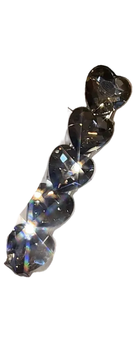 A set of five heart-shaped clear rhinestones attached to a white display card, held by a hand with glittery nail polish in a blurred indoor setting.