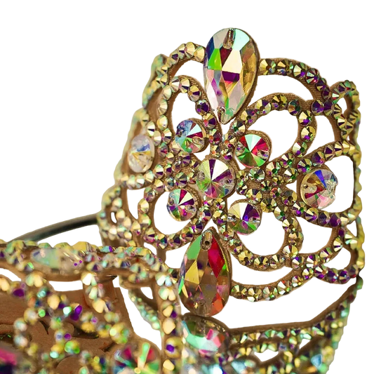 A close-up of an ornate gold crown embellished with iridescent rhinestones that reflect rainbow colors, set against a soft beige background.