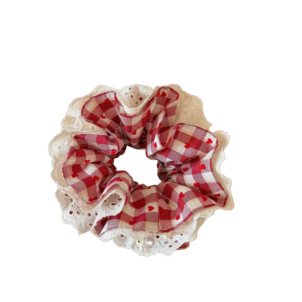 A fabric hair scrunchie with a red and white gingham pattern and a white lace trim, resting on a beige book on a wooden table.