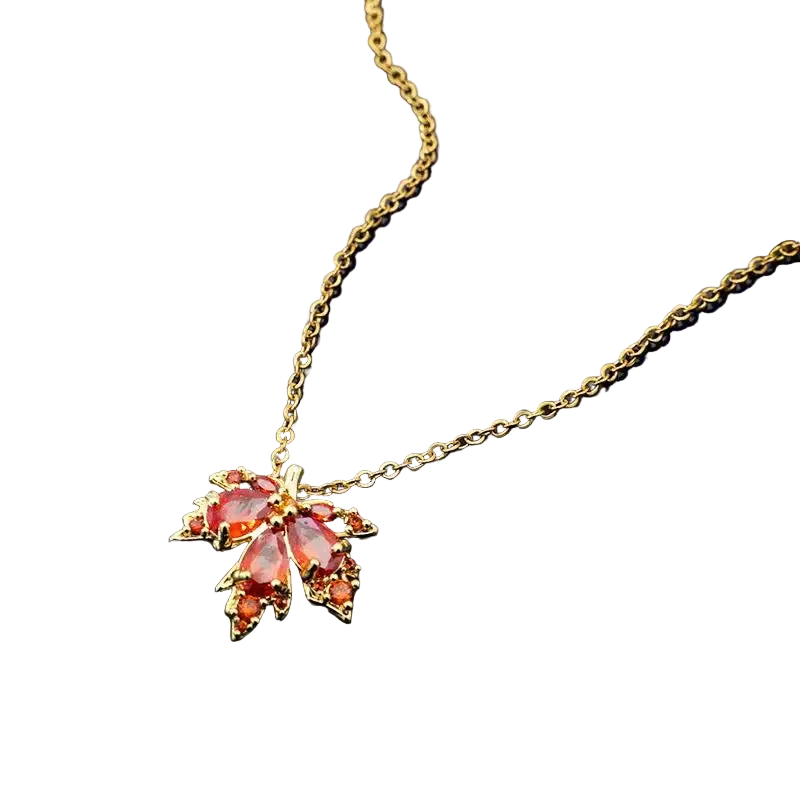 Gold necklace with a leaf-shaped pendant featuring red and pink gemstones on a dark background.