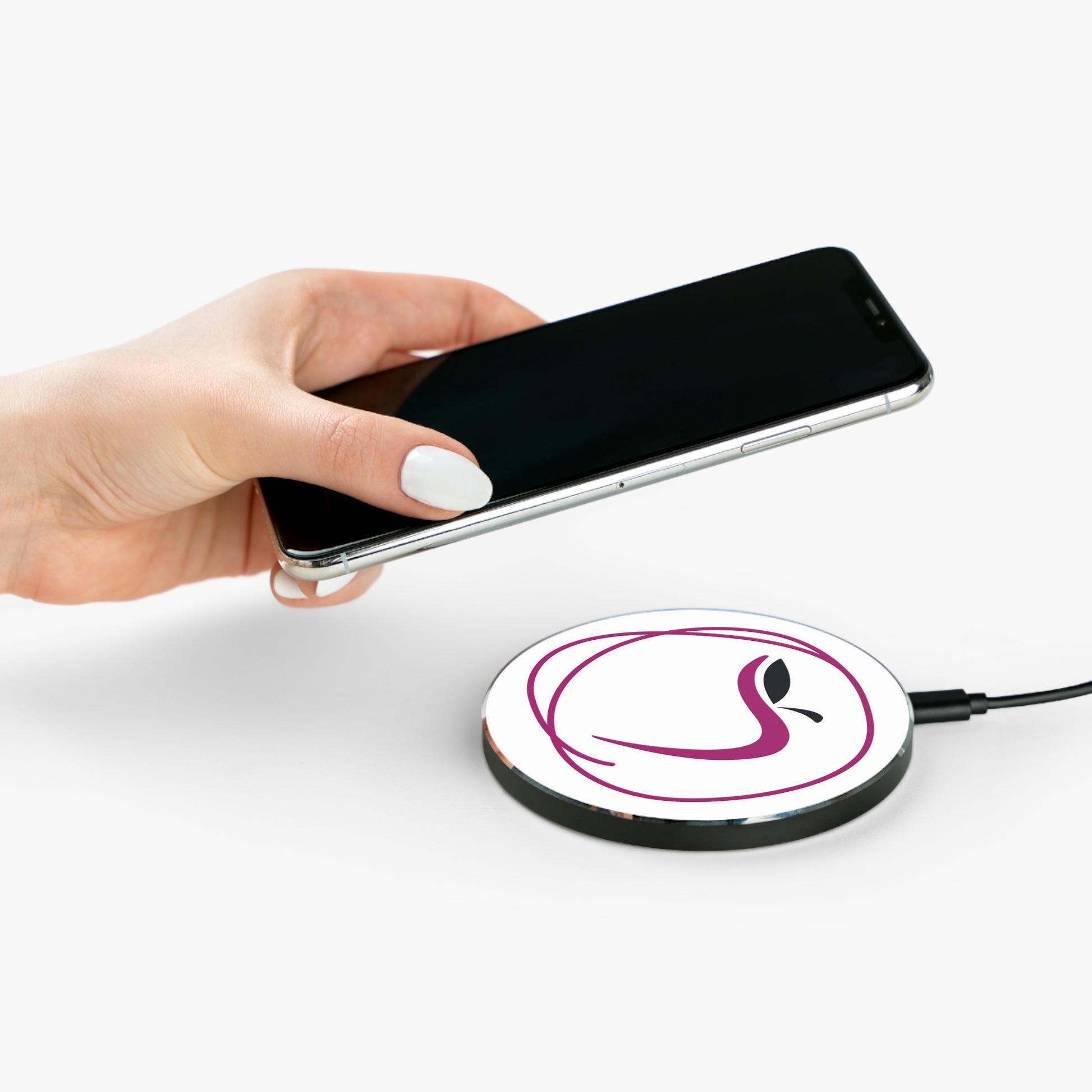 Hand holding a smartphone above a wireless charging pad with a logo on a white background