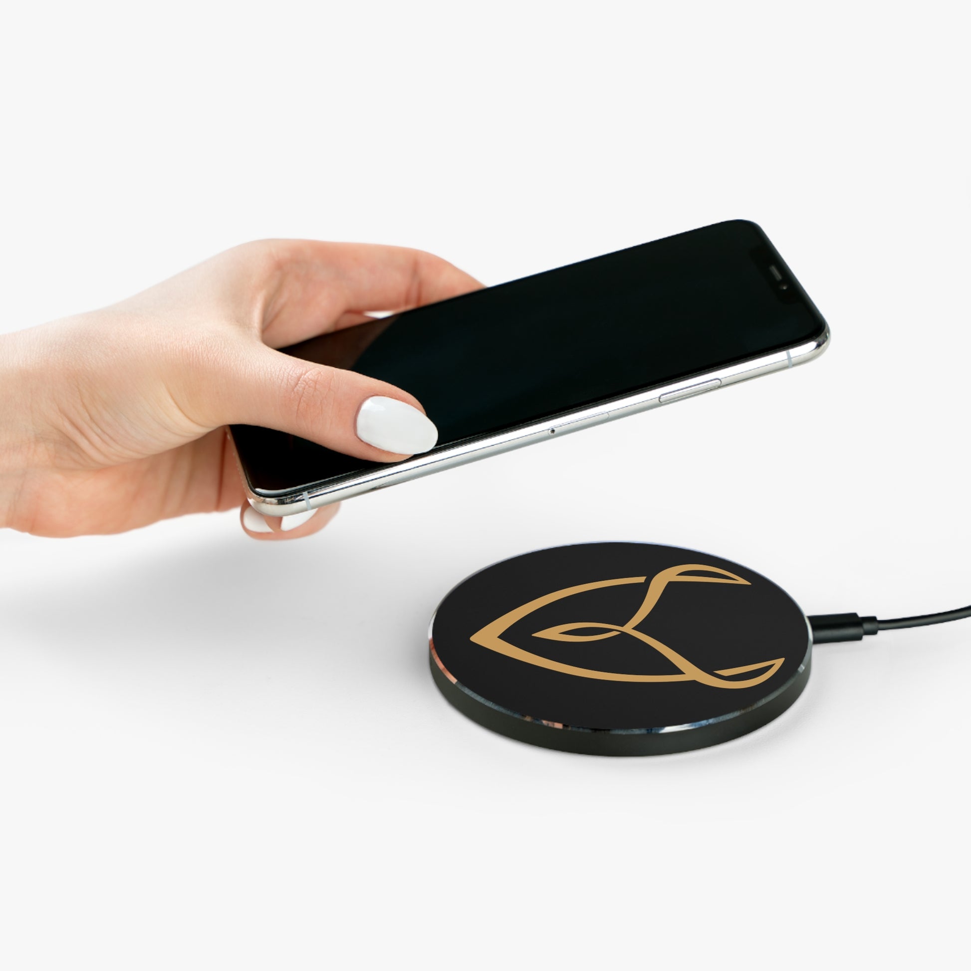 Hand holding a smartphone above a wireless charging pad with a logo on a white background