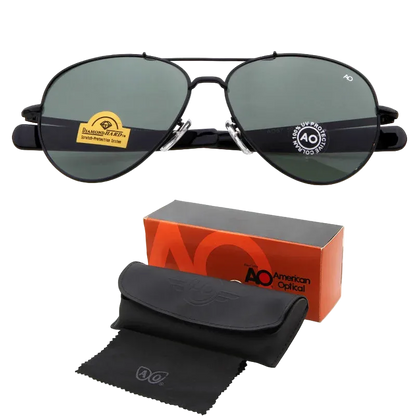 Black aviator sunglasses with dark green lenses, shown with an orange and black AO American Optical box, a black hard case, and a black microfiber cloth on a white background.