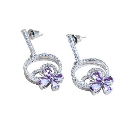 Silver earrings with purple gemstones on a light wooden surface, featuring '925 Sterling Silver' text.