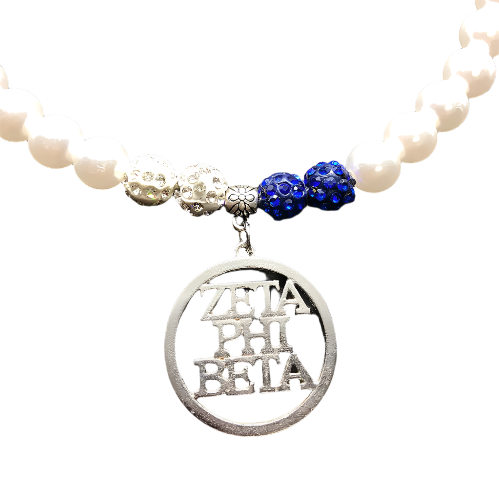Necklace with white beads, blue and silver charms, and a Zeta Phi Beta pendant on a dark background.