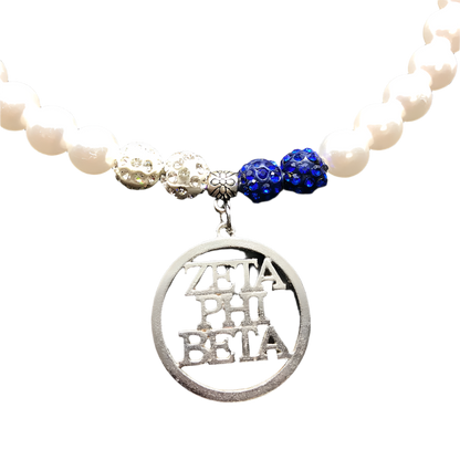 Necklace with white beads, blue and silver charms, and a Zeta Phi Beta pendant on a dark background.