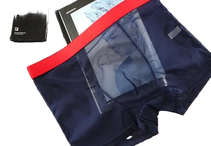 Navy blue boxer briefs with red waistband on a wooden surface, with a pen and small box in the background.