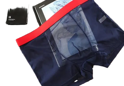 Navy blue boxer briefs with red waistband on a wooden surface, with a pen and small box in the background.