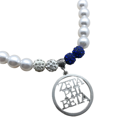 Pearl necklace with blue beads and a 'Zeta Phi Beta' charm on a wooden surface
