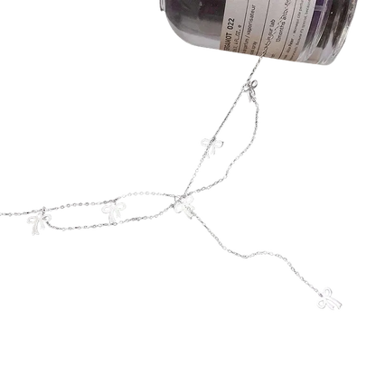 A delicate silver chain necklace featuring five small bow-shaped charms, displayed on a black background with a bottle partially visible at the top right.