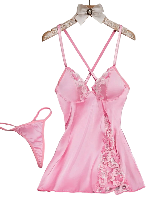 Pink satin nightgown with lace details on a hanger against a white wall.
