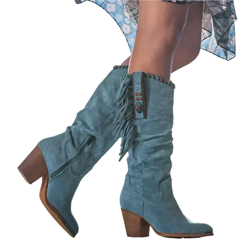 Blue suede boots with fringe details worn by a person against a blurred natural background