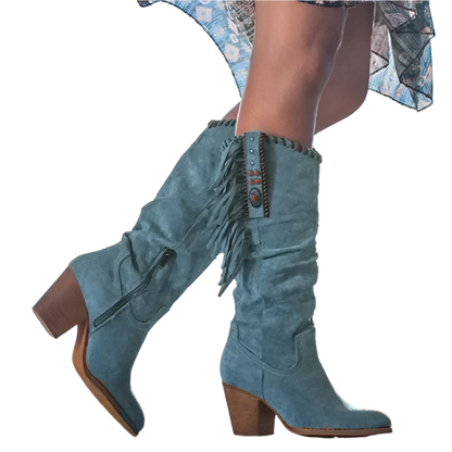 Blue suede boots with fringe details worn by a person against a blurred natural background