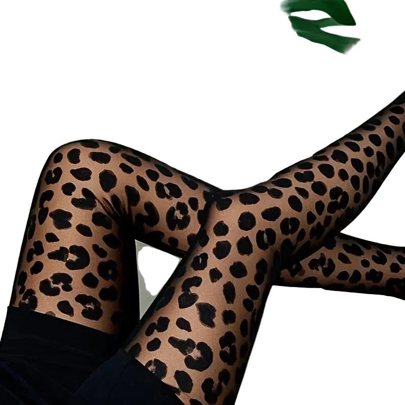 A person wearing sheer leopard-print tights with black spots, posed with crossed legs on a white surface with large green monstera leaves in the background.