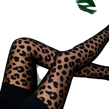 A person wearing sheer leopard-print tights with black spots, posed with crossed legs on a white surface with large green monstera leaves in the background.