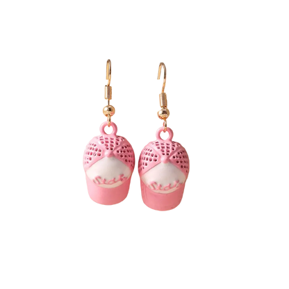 A pair of dangling earrings displayed on a beige jewelry bust. Each earring has a gold fishhook wire and a pink charm shaped like a cupcake, with a pink lace-knit top and a white cake body featuring pink frosting details.