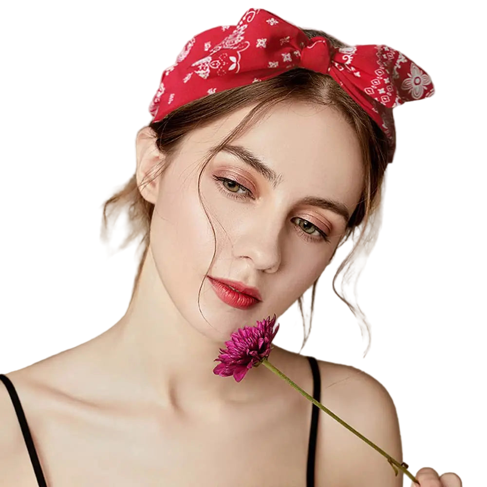 Woman wearing a red bandana with floral patterns, holding a purple flower against a beige background