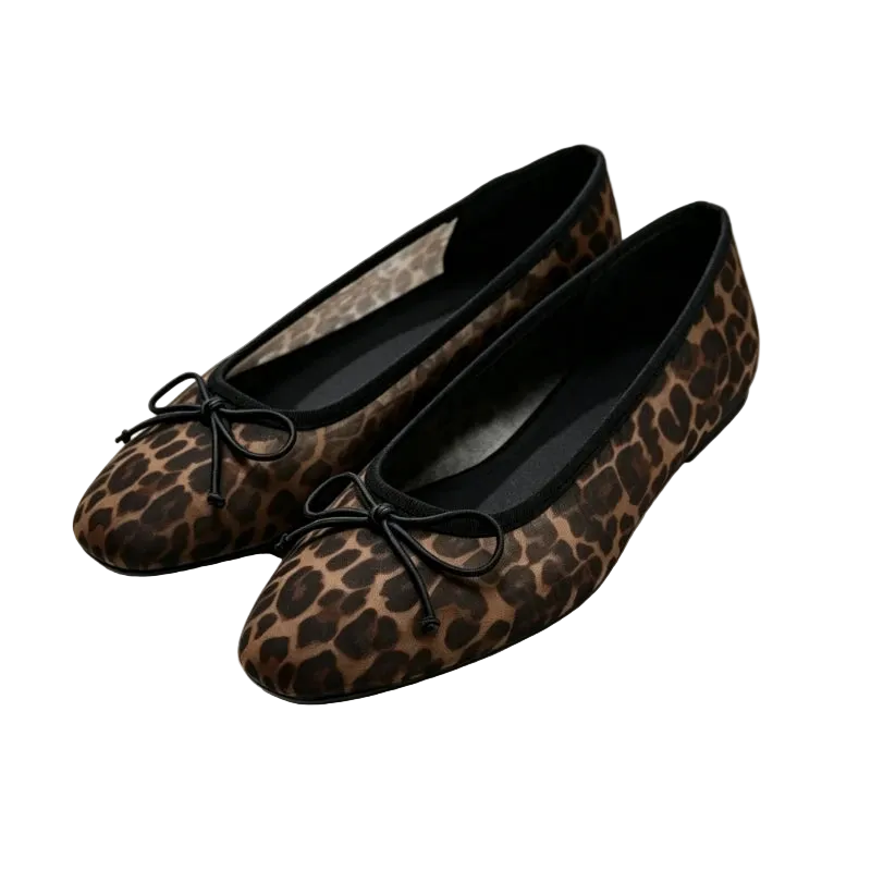 A pair of women's flat ballet flats in a brown and black leopard print, featuring black fabric bows on the toes, displayed on a white platform.