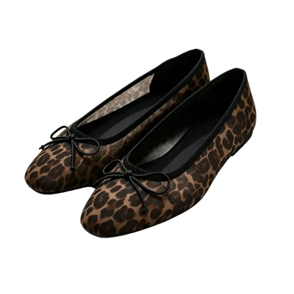 A pair of women's flat ballet flats in a brown and black leopard print, featuring black fabric bows on the toes, displayed on a white platform.