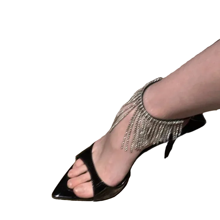 Black high-heeled sandal with fringe detail on a marble floor