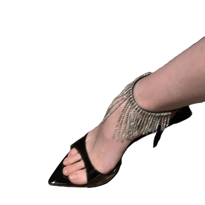 Black high-heeled sandal with fringe detail on a marble floor