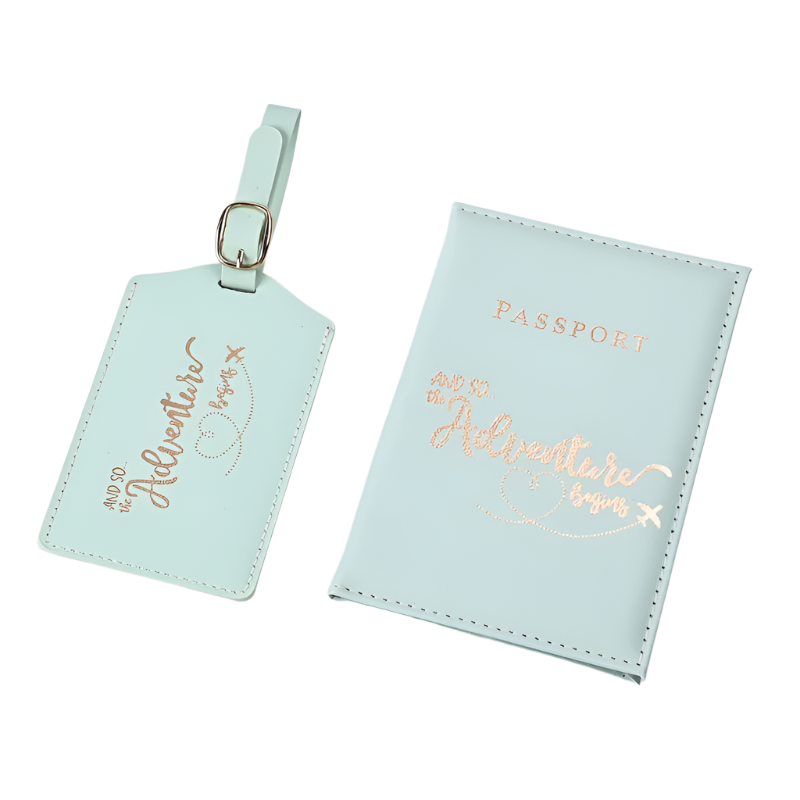 A passport holder and luggage tag set with the phrase "And so the adventure begins" in elegant script. The design is sleek and stylish, perfect for travel.