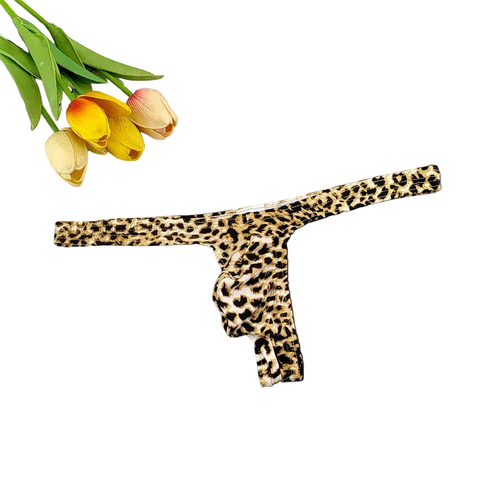 A leopard print thong underwear piece laid flat on a dark surface, with tulips and a white tiled corner used as styling props.
