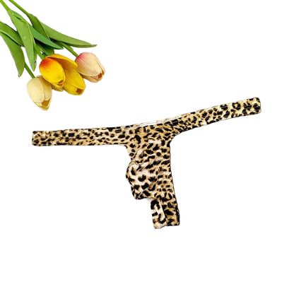 A leopard print thong underwear piece laid flat on a dark surface, with tulips and a white tiled corner used as styling props.