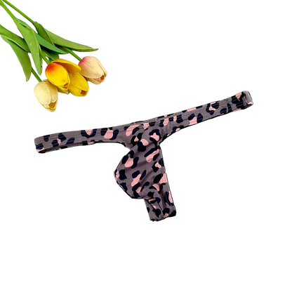 A single thong-style underwear piece with a dark gray base and pink and black leopard print, laid flat on a dark surface with tulips and a white grid tile as styling props.