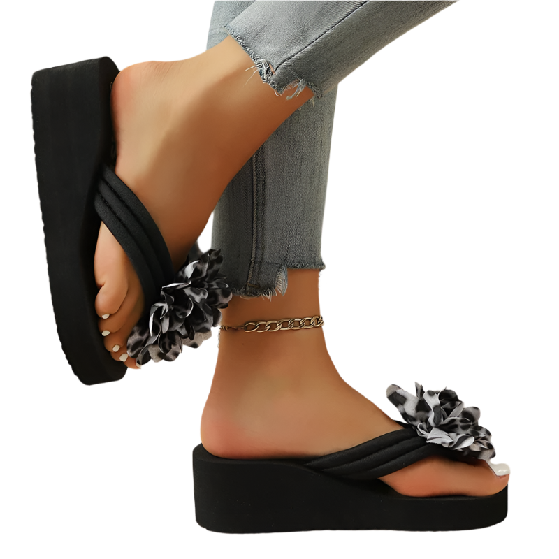 Black wedge sandals with floral details worn by a person on a wooden floor.