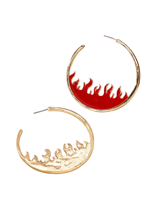 A pair of gold crescent-shaped hoop earrings with flame designs, one featuring a smooth red flame pattern and the other a textured gold flame pattern, displayed on a cream satin fabric next to a wooden jewelry box.
