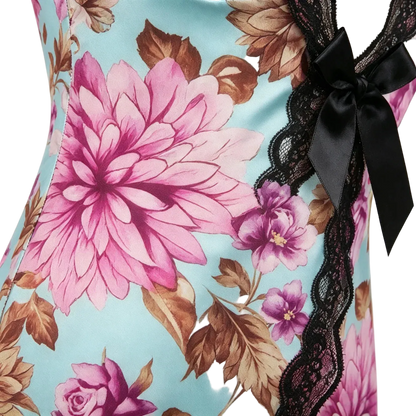 Close-up of a floral bodysuit or dress with a light blue background, large pink flowers, brown leaves, black lace trim, and a black satin bow.