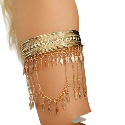 A gold-toned armband jewelry piece with multiple layered chains and dangling leaf-shaped charms, shown worn on a model's upper arm against a light neutral background.