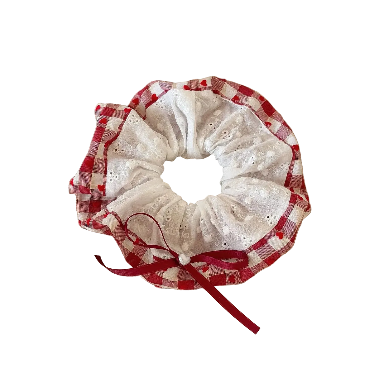 A fabric hair scrunchie with a red and white gingham border, white eyelet lace center, and a red ribbon bow, resting on a beige book on a wooden table.