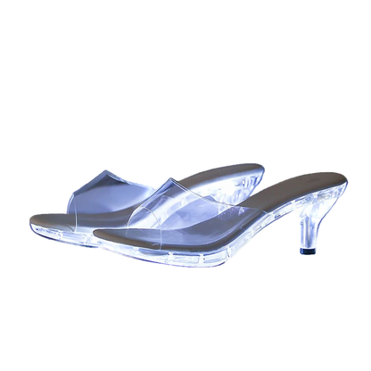 Clear high-heeled shoes with glowing sole on a reflective surface