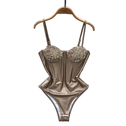 Gold swimsuit with embellishments on a hanger against a decorative background with flowers and a hat.