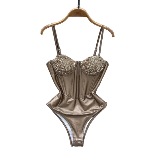 Gold swimsuit with embellishments on a hanger against a decorative background with flowers and a hat.