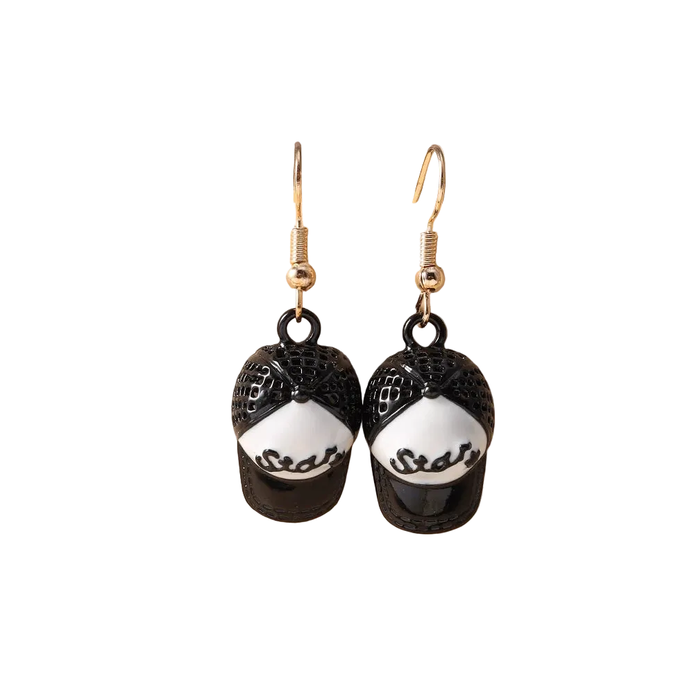 A pair of dangling earrings shaped like black baseball caps with white panels and black script lettering, hanging from gold hooks on a beige display stand.