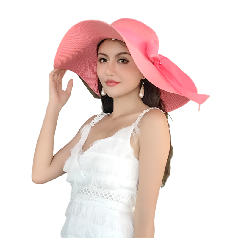 Woman wearing a large pink hat and white dress outdoors with greenery.