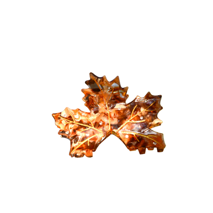 A decorative glass leaf sculpture made from an orange-brown oak leaf, mounted on a tree branch outdoors with a blurred natural background.