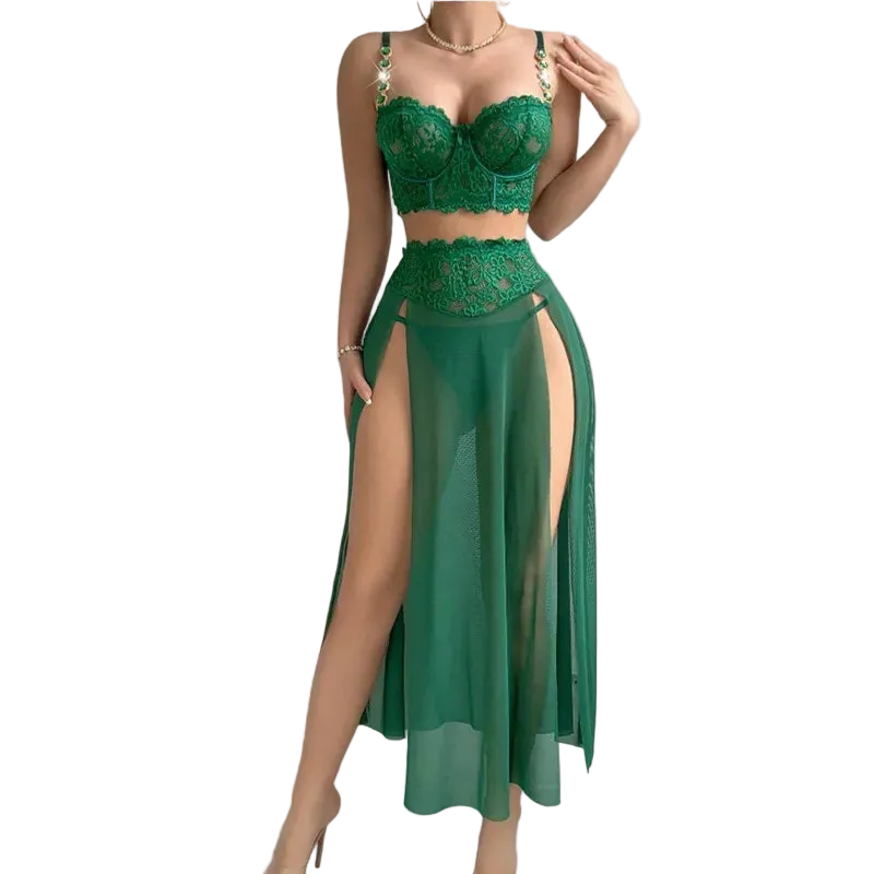 A woman models a two-piece green lace and sheer maxi dress set against a solid gray background. The set includes a green lace bralette with gold chain straps and a matching high-waisted sheer skirt with a thigh-high slit.