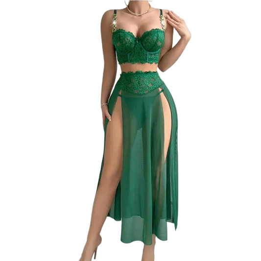 A woman models a two-piece green lace and sheer maxi dress set against a solid gray background. The set includes a green lace bralette with gold chain straps and a matching high-waisted sheer skirt with a thigh-high slit.